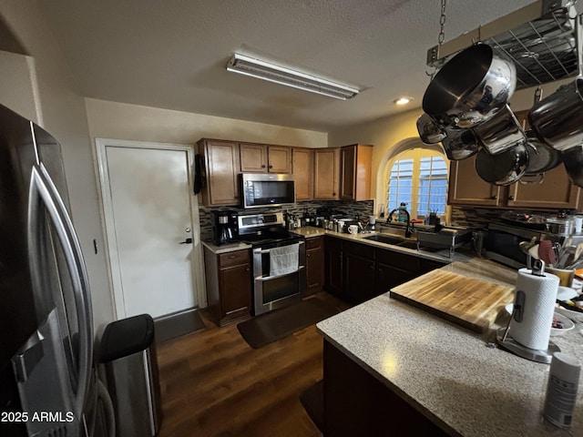 kitchen with pendant lighting, sink, dark wood-type flooring, appliances with stainless steel finishes, and tasteful backsplash