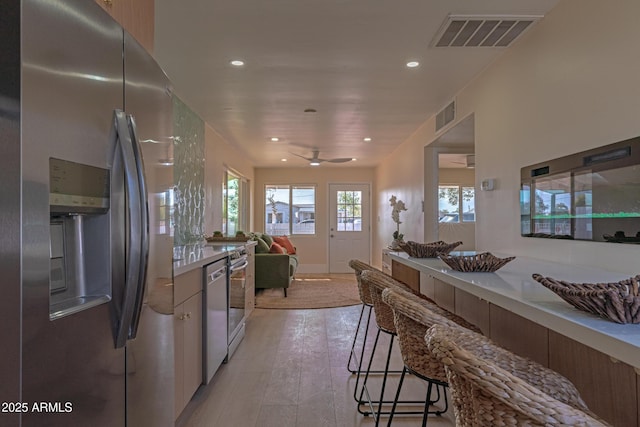 kitchen with ceiling fan, stainless steel appliances, a kitchen bar, and light wood-type flooring