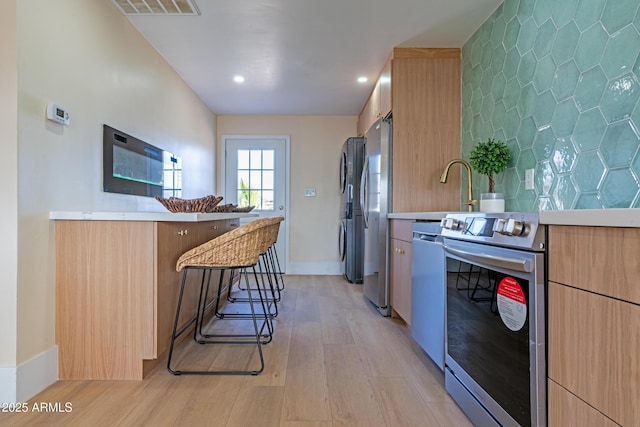 kitchen with sink, a breakfast bar area, kitchen peninsula, stainless steel appliances, and light hardwood / wood-style flooring