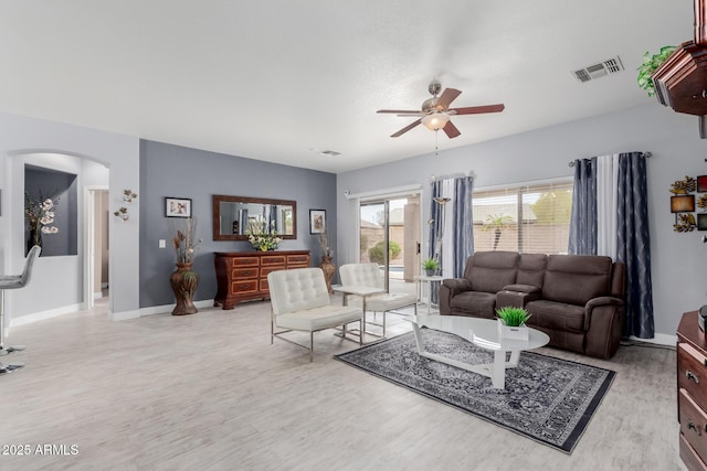 living room with baseboards, visible vents, light wood-style flooring, arched walkways, and ceiling fan