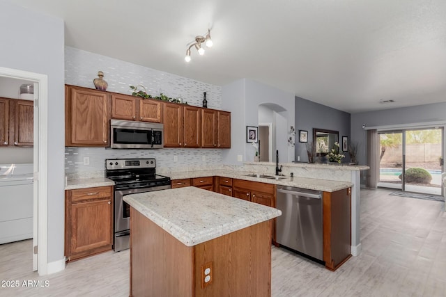 kitchen featuring washer / dryer, a peninsula, arched walkways, a sink, and stainless steel appliances