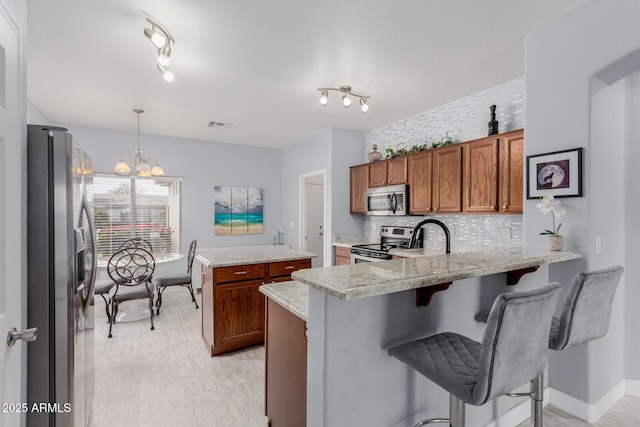 kitchen with decorative backsplash, brown cabinets, a peninsula, a notable chandelier, and stainless steel appliances