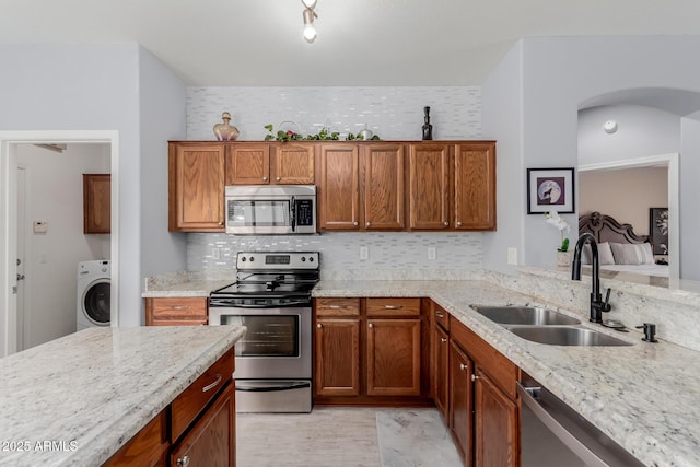 kitchen featuring brown cabinets, a sink, washer / clothes dryer, stainless steel appliances, and light stone countertops