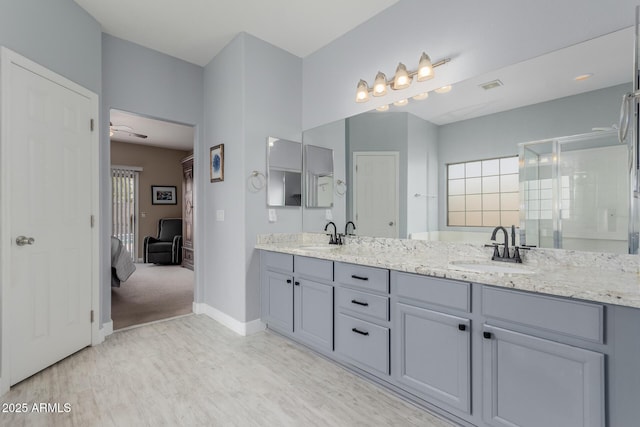 bathroom featuring visible vents, a shower stall, double vanity, wood finished floors, and a sink