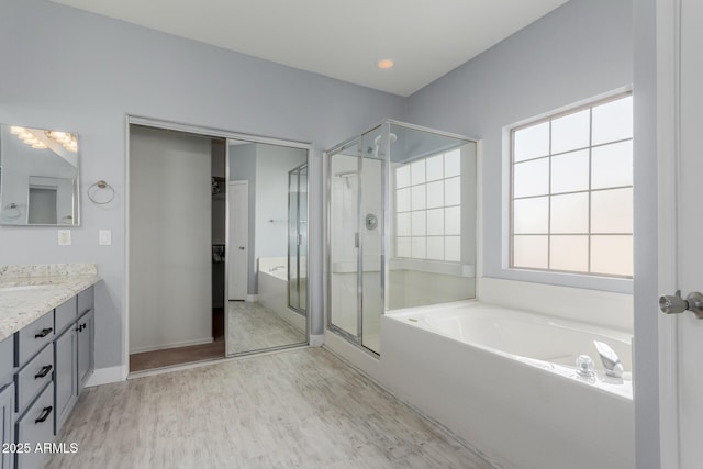 bathroom with a stall shower, wood finished floors, baseboards, a bath, and vanity