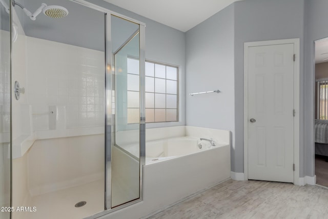 ensuite bathroom featuring wood finished floors, baseboards, ensuite bath, a stall shower, and a bath