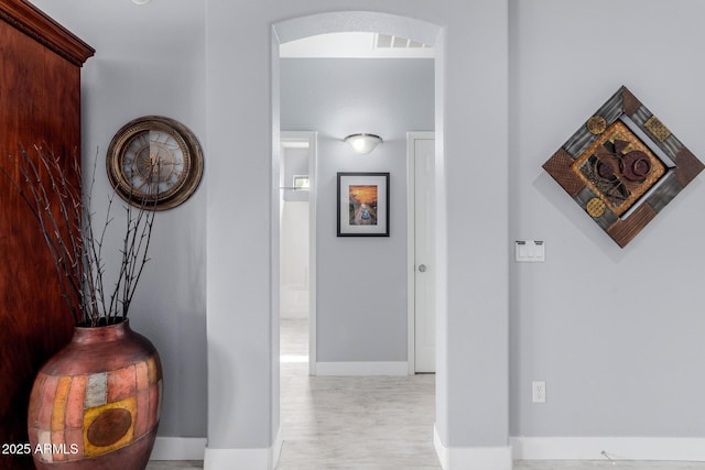 corridor with wood finished floors, visible vents, arched walkways, and baseboards