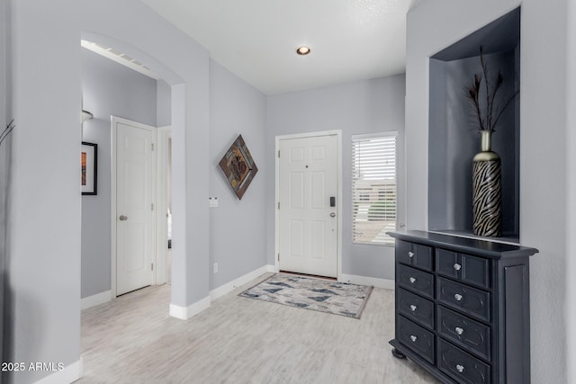 foyer entrance featuring baseboards, arched walkways, and light wood-style floors