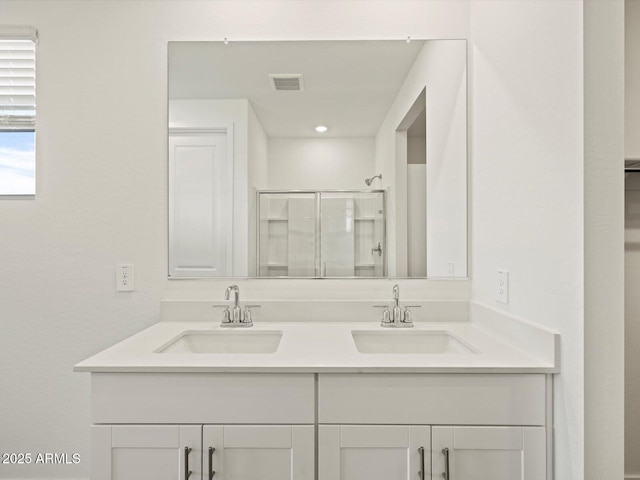 full bath featuring double vanity, a shower stall, visible vents, and a sink