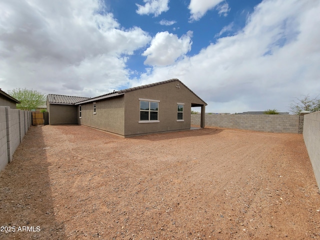 rear view of property with a fenced backyard, a tiled roof, and stucco siding