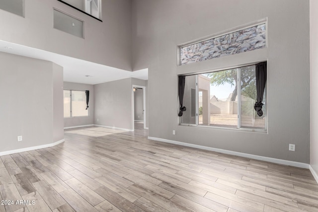 unfurnished living room featuring a wealth of natural light, light hardwood / wood-style flooring, and a towering ceiling