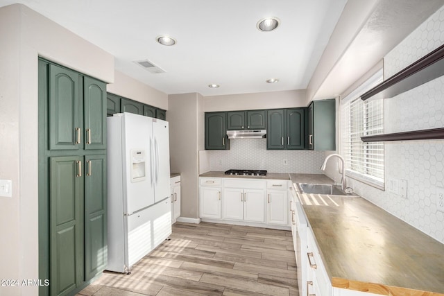 kitchen with decorative backsplash, white cabinetry, white fridge with ice dispenser, and sink