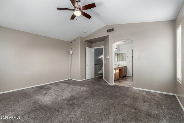 unfurnished bedroom with ceiling fan, dark carpet, lofted ceiling, and connected bathroom