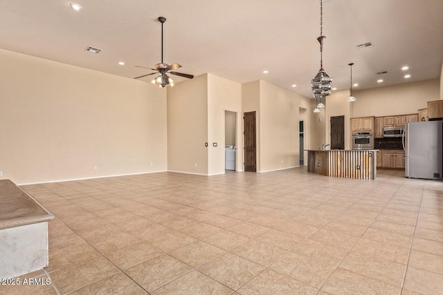 interior space featuring hanging light fixtures, appliances with stainless steel finishes, ceiling fan, washer / clothes dryer, and a kitchen island with sink