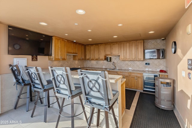 kitchen featuring sink, wine cooler, light stone counters, a kitchen bar, and light tile patterned flooring