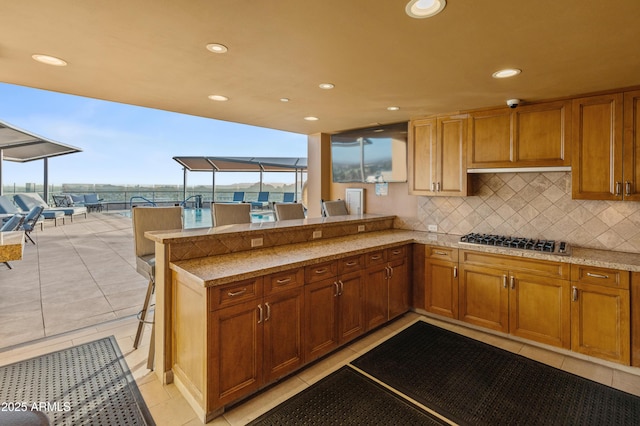 kitchen with a kitchen bar, kitchen peninsula, backsplash, light tile patterned floors, and stainless steel gas stovetop