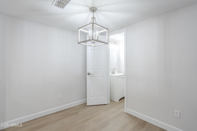 unfurnished dining area with baseboards, an inviting chandelier, a sink, and light wood-style floors