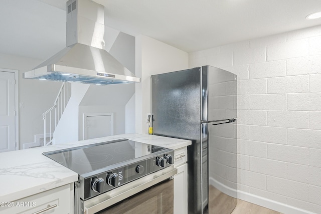 kitchen featuring light stone counters, range with electric cooktop, light wood finished floors, wall chimney exhaust hood, and freestanding refrigerator