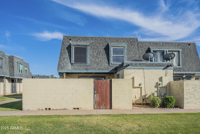back of house featuring a gate, a fenced front yard, a yard, mansard roof, and roof with shingles
