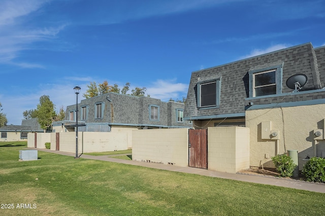 back of house with a yard, a shingled roof, mansard roof, and fence