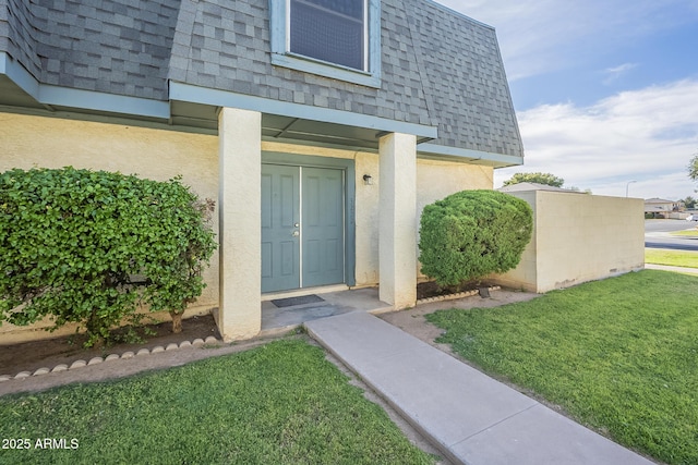 doorway to property featuring a lawn, roof with shingles, mansard roof, and stucco siding