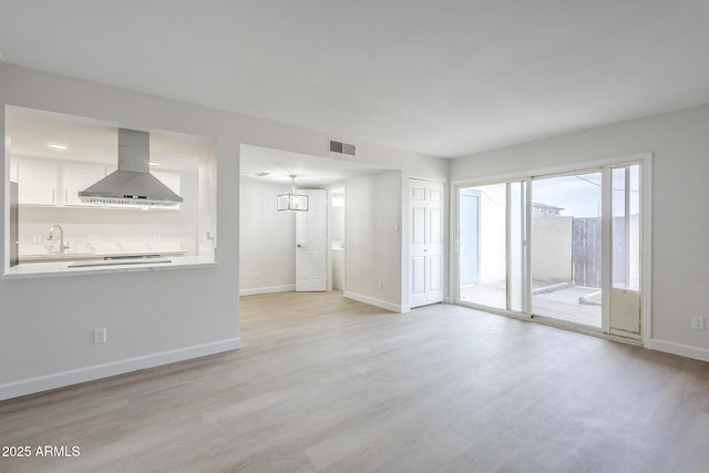 unfurnished living room featuring baseboards, a sink, visible vents, and light wood-style flooring