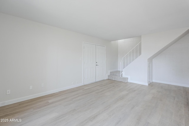 unfurnished living room with stairway, baseboards, and light wood-style floors