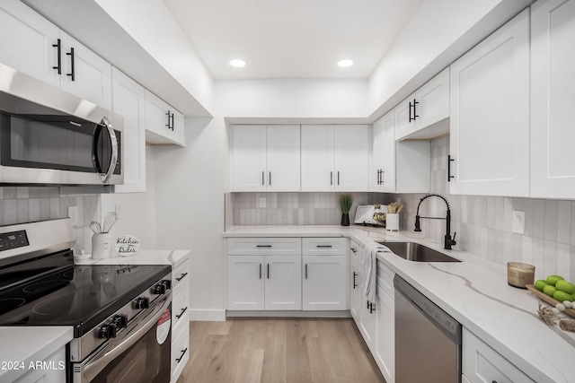 kitchen featuring sink, appliances with stainless steel finishes, decorative backsplash, white cabinets, and light wood-type flooring