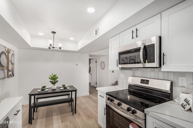 kitchen featuring appliances with stainless steel finishes, pendant lighting, an inviting chandelier, light hardwood / wood-style flooring, and white cabinetry