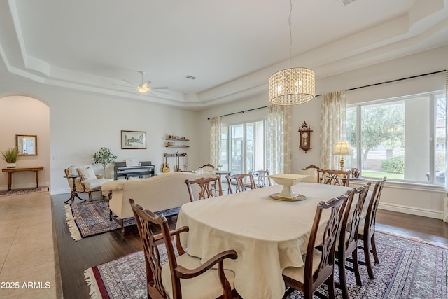 dining area featuring ceiling fan with notable chandelier, a tray ceiling, plenty of natural light, and hardwood / wood-style flooring