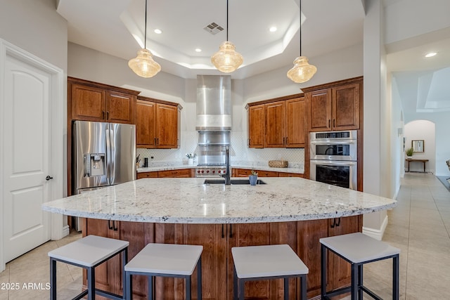 kitchen featuring backsplash, a center island with sink, sink, appliances with stainless steel finishes, and a tray ceiling