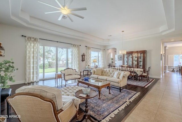 living room featuring a raised ceiling, ceiling fan, and light tile patterned flooring