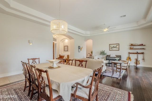 dining room with a tray ceiling, dark wood-type flooring, and ceiling fan with notable chandelier