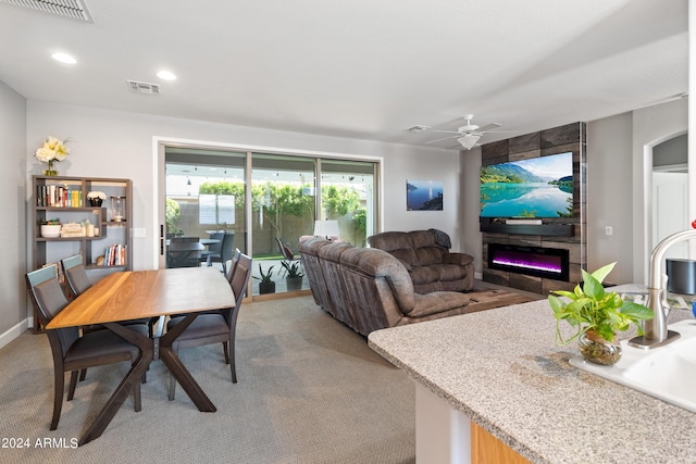 carpeted living room featuring a large fireplace and ceiling fan