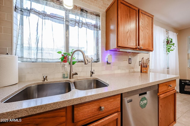 kitchen featuring a sink, stainless steel dishwasher, brown cabinetry, decorative backsplash, and light stone countertops