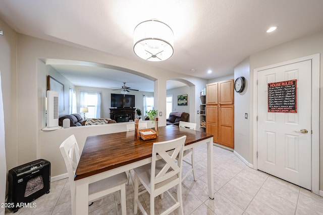 dining area with baseboards, light tile patterned floors, recessed lighting, arched walkways, and a glass covered fireplace