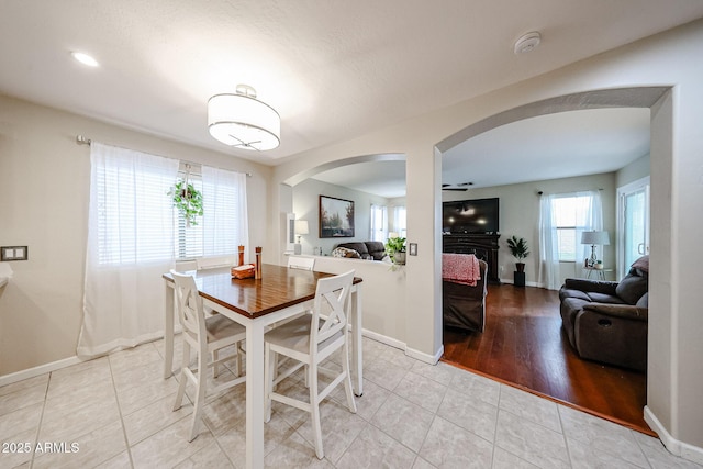 dining area featuring arched walkways, light tile patterned floors, a fireplace, and baseboards