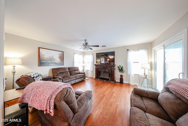 living area with baseboards, light wood-style floors, a glass covered fireplace, and a ceiling fan