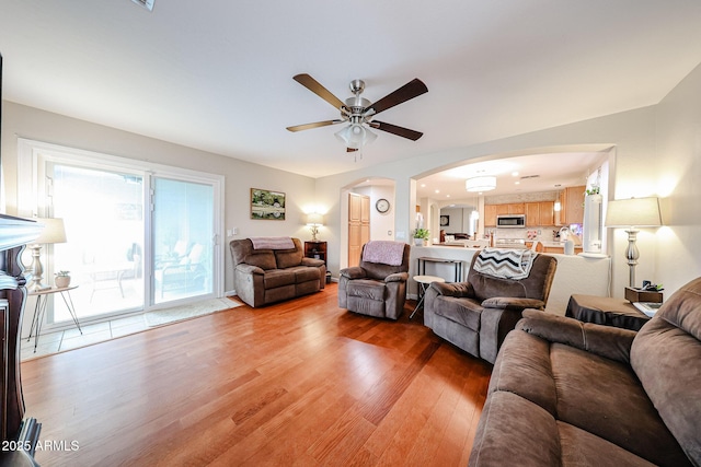 living room featuring arched walkways, a ceiling fan, and light wood-style floors