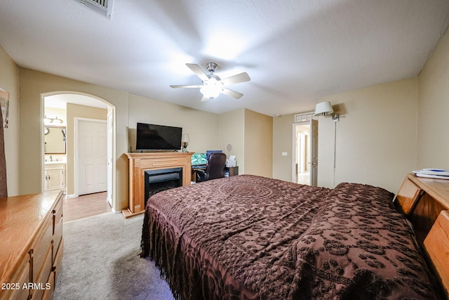 bedroom with visible vents, a ceiling fan, arched walkways, a fireplace, and light colored carpet