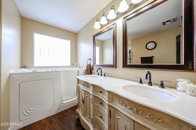 full bath featuring visible vents, wood finished floors, a garden tub, and a sink