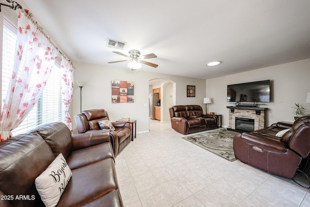 living area with visible vents, baseboards, a stone fireplace, arched walkways, and a ceiling fan