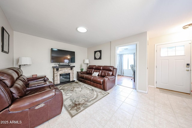 living room featuring light tile patterned floors, a stone fireplace, and baseboards