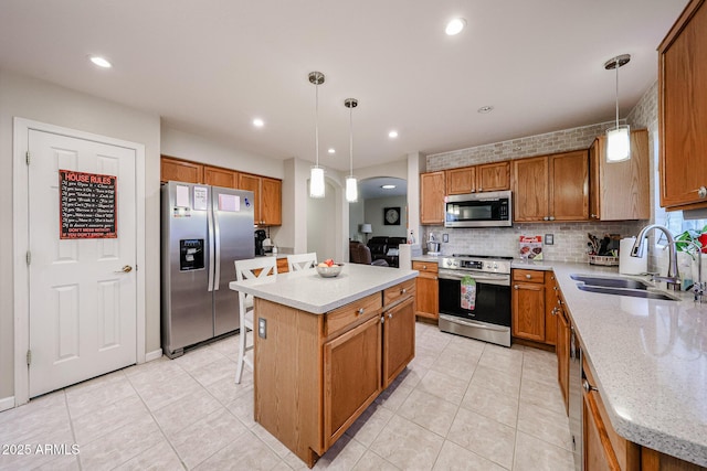 kitchen with brown cabinetry, a kitchen island, a sink, appliances with stainless steel finishes, and tasteful backsplash