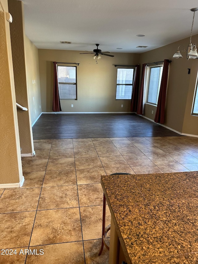 spare room featuring dark hardwood / wood-style floors, ceiling fan with notable chandelier, and plenty of natural light