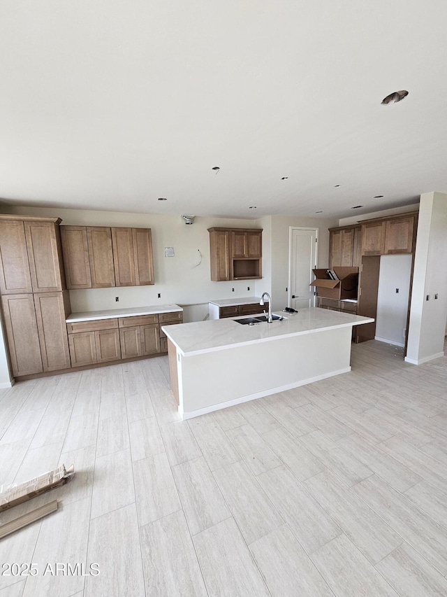 kitchen with a sink, a kitchen island with sink, and brown cabinetry
