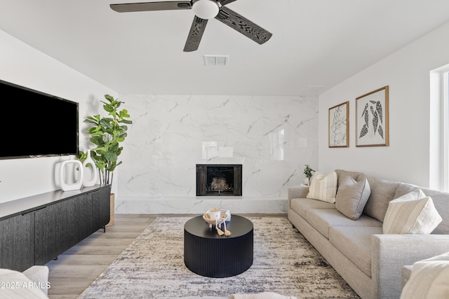 living room featuring a premium fireplace, ceiling fan, and light hardwood / wood-style floors