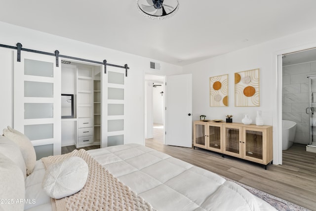 bedroom with ensuite bathroom, wood-type flooring, and a barn door