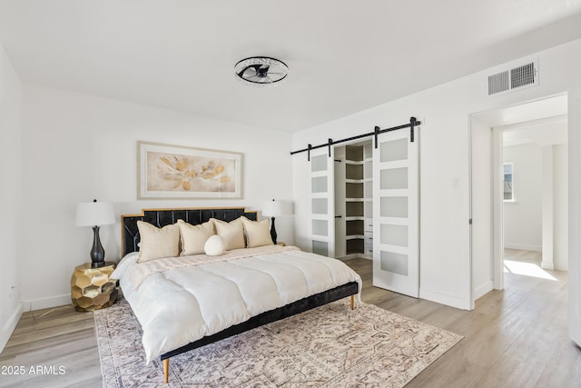 bedroom with a barn door and light hardwood / wood-style floors