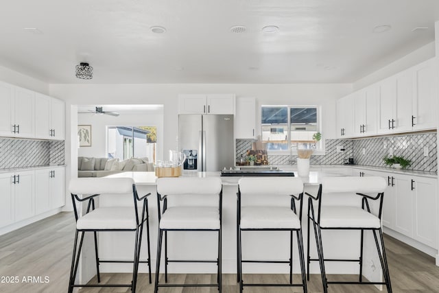 kitchen featuring stainless steel refrigerator with ice dispenser, a kitchen island, backsplash, white cabinets, and a kitchen breakfast bar